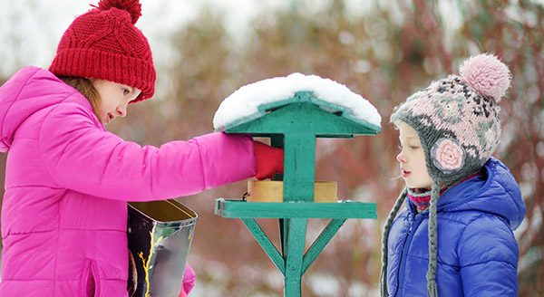 Two adorable sisters feeding birds on chilly winter day in city park. Children helping birds at winter.